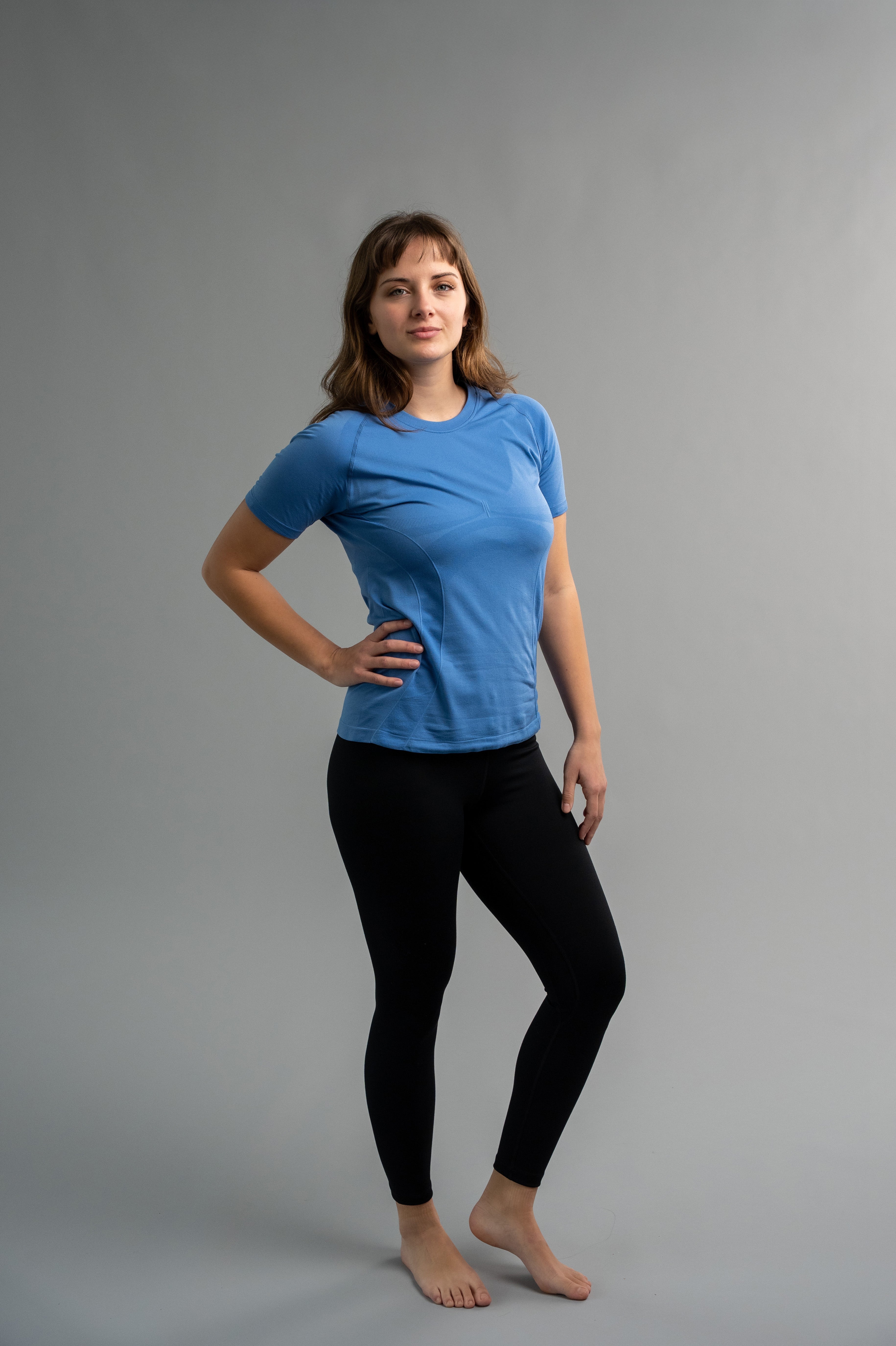 Woman wearing a blue t-shirt and black leggings against a gray background