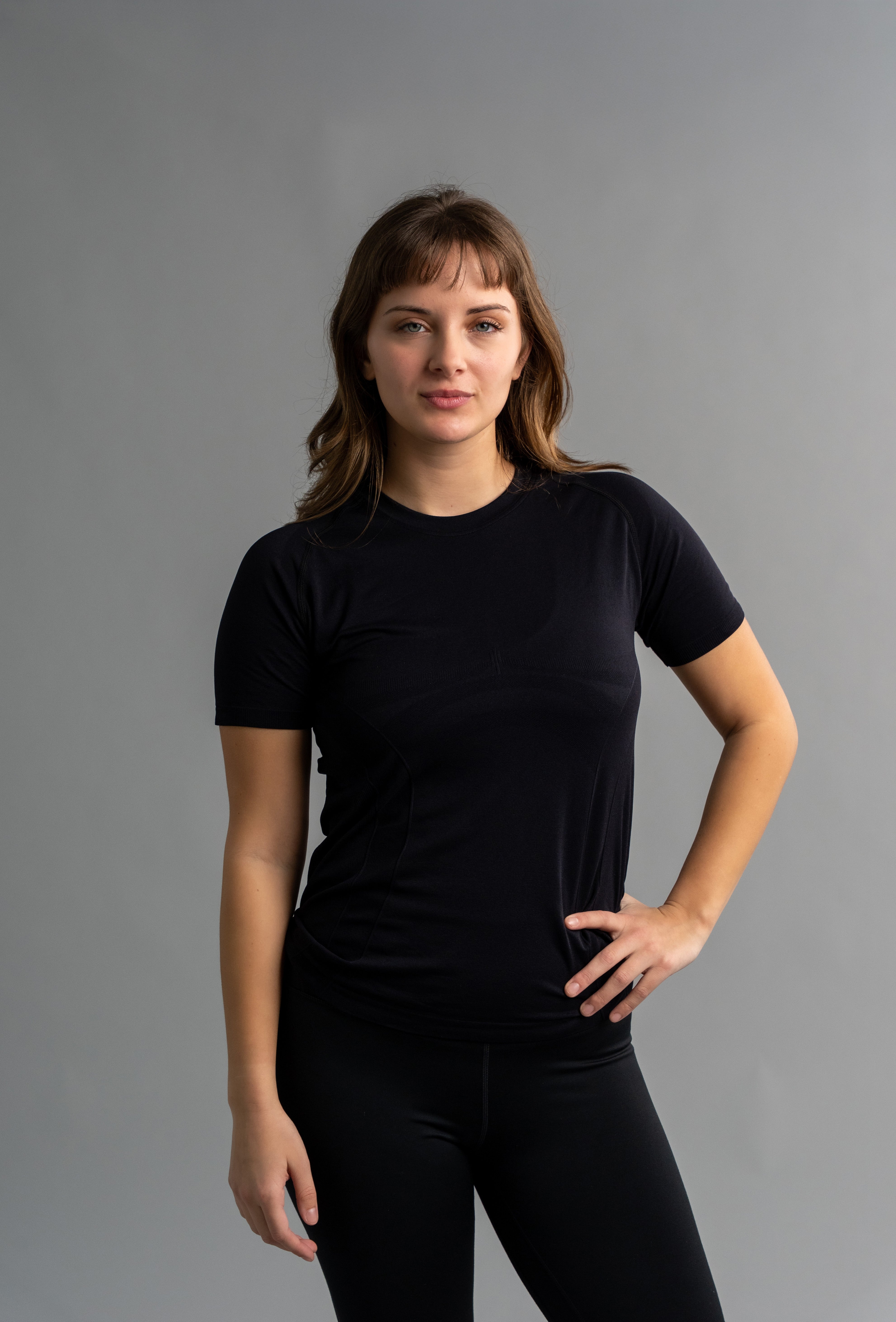 Woman wearing a black t-shirt and pants against a gray background